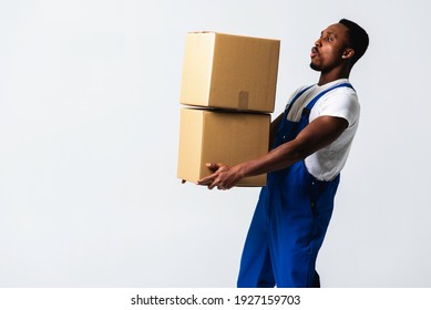 Courier With A Paper Box, A Young African American Man In A Blue Jumpsuit And A White T-shirt Holding Craft Paper Boxes For Sending. Isolated On A White Background. The Concept Of Delivery, Mail, Ship