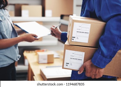 Courier With Parcels Signing Document In Delivery Service Office