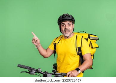 Courier pointing upwards on a bike with yellow backpack, wearing helmet. Concept of guidance or direction. Green background. - Powered by Shutterstock