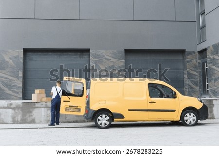Courier preparing parcels for delivery, loading cardboard boxes into a yellow van parked outside a warehouse
