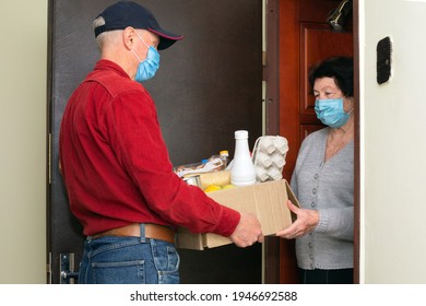 Courier With Protect Face Mask Delivering Shopping To Senior Woman With Face Mask, Corona Virus And Quarantine Concept. Donation Box With Foods, Meals.