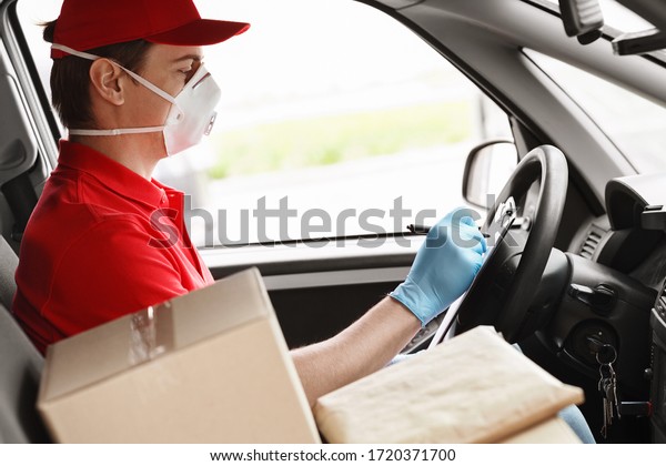 Courier in protective mask in car writes to tablet,\
near cardboard boxes