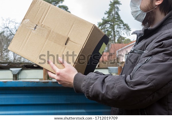 Courier in protective mask delivers parcel, car\
delivery service under quarantine, disease outbreak, coronavirus\
pandemic conditions. close-up of cardboard box holding by a male\
courier in white hat