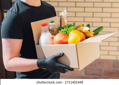 The Courier In Protective Mask And Gloves Delivers Box Of Different Food. Food Delivery During Corona Virus Outbreak. Safe Home Delivery. Takeout Meal. 