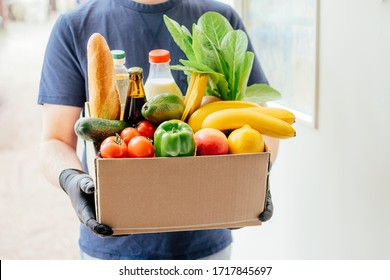 The Courier In Protective Mask And Gloves Delivers Box Of Different Food. Food Delivery During Virus Outbreak. Safe Home Delivery. Takeout Meal. 