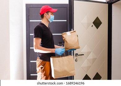 Courier In Protective Mask And Medical Gloves Delivers Takeaway Food. Delivery Service Under Quarantine, Disease Outbreak, Coronavirus Covid-19 Pandemic Conditions.