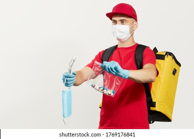 A Courier In A Red Uniform, Protective Mask And Gloves Delivers Pill Drug And Thermometer. Stay At Home And Take Care Of Your Health. Courier Drug Delivery