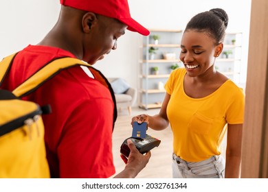 Courier Service. Cheerful Female Customer Paying Deliveryman With Credit Card For Food Delivery Standing At Home. Payment For Meal Delivery Concept. Selective Focus