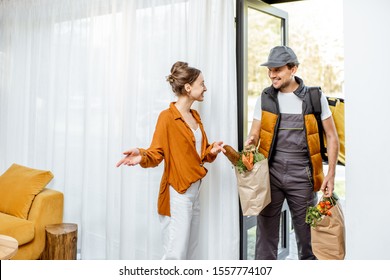 Courier In Uniform Delivering Fresh Groceries Home For A Young Client. Online Shopping And Home Delivery Concept