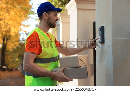 Courier in uniform with parcels ringing doorbell outdoors