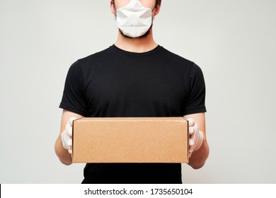 Courier wearing a protective mask and medical gloves holds a box on an isolated white background - Shutterstock ID 1735650104