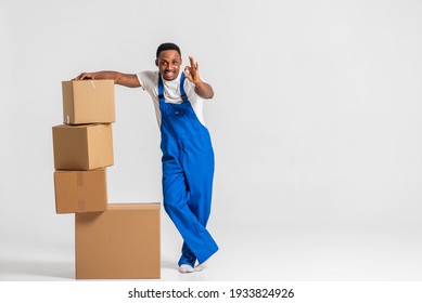 courier, a young African-American in a blue jumpsuit and white T-shirt, tired, standing near the paper boxes folding them, working. Isolated on white background. The concept of delivery, mail, deliver