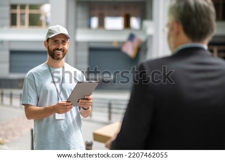 A courrier in a cap giving a box to the man in a suuit