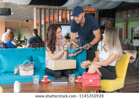 Courrier delivering the package to the girls in the coffe shop while they are drinking coffe.