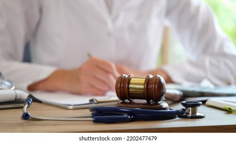 Court gavel with stethoscope on a table in background doctor writes notes. Concept of medical law and medical crimes - Shutterstock ID 2202477479