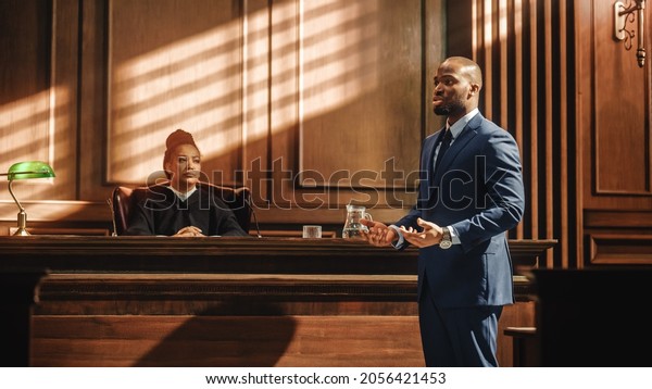 Court of Justice and Law Trial: Male Public\
Defender Presenting Case, Making Passionate Speech to Judge, Jury.\
African American Attorney Lawyer Protecting Client\'s Innocents with\
Supporting Argument.