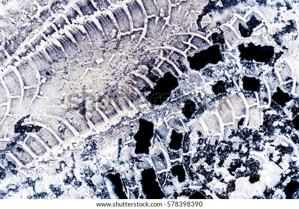 Cover manhole covered by\
snow and trace of car tires. Close up view from above, image in the\
blue tones