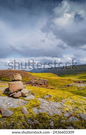 Cover page with Icelandic colorful and wild landscape with lava field covered by ancient moss with stacked stones as a cairns at dramatic rainy sky, Iceland
