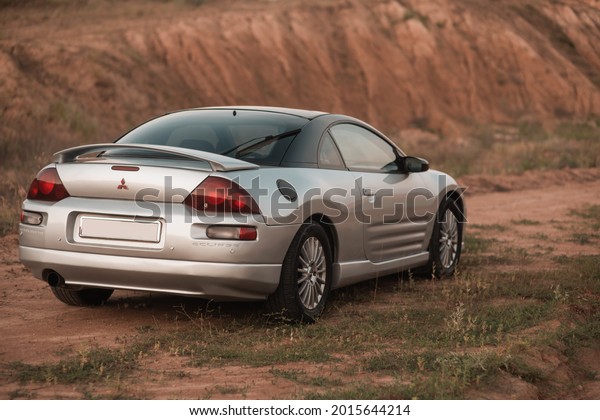 Cover, Ukraine - July, 23 2021: test drive of the\
American car coupe sports car Mitsubishi Eclipse gray among the\
mountains. Front view. Close-up. Beautiful car on the road with\
warm sunlight 