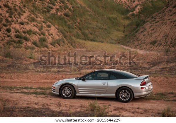 Cover, Ukraine - July, 23 2021: test drive of\
the American car coupe sports car Mitsubishi Eclipse gray among the\
mountains. Front view. Close-up. Beautiful car on the road with\
warm sunlight