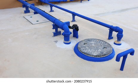 Cover For Underground Water Tanks And Pipes. Reserve Water Tank System With Blue Water Pipes And Ventilation Pipes On A Cement Background. Selective Focus