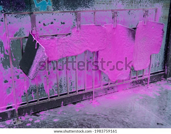 Covered auto mats with pink foam at a\
self-service car wash. car wash with a spray of magenta soap from a\
pistol. Cleaning car mats with a foam gun in the manual\
self-service washing\
station.