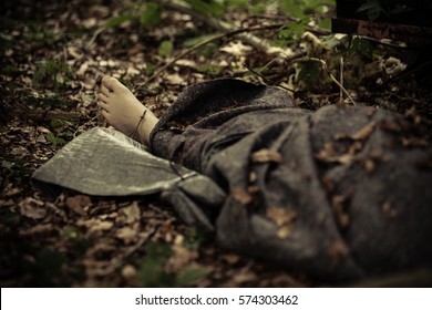 Covered corpse of murder victim with bare feet protruding lying in leafy forest - Shutterstock ID 574303462