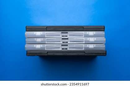 Covered DVD cases are lined up side by side. Transparent and black movie DVD boxes. Blue Background, top angle.
