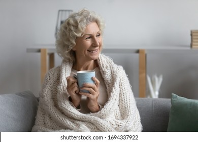 Covered in knitted warm plaid happy senior middle aged woman relaxing on comfortable couch with cup of morning strong black coffee or enjoying cozy lazy weekend evening with mug of hot tea at home. - Powered by Shutterstock