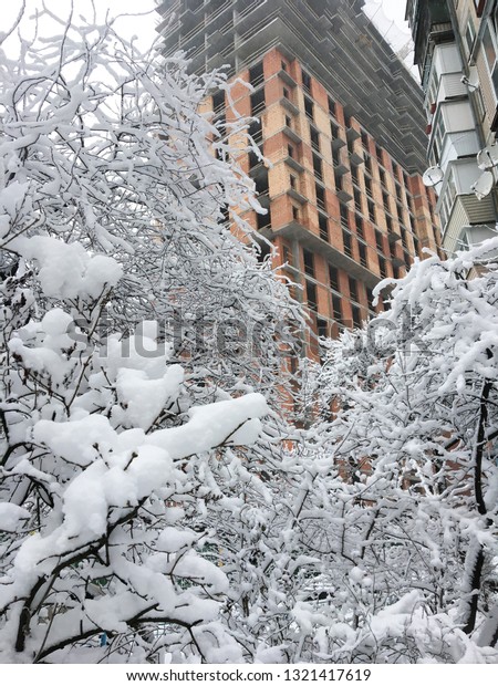 Covered in white snow with snow banks. Winter in the\
city. High houses in the background. Building. Snow covered trees\
in the city