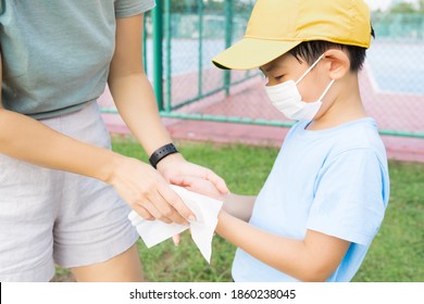 Covid 19 New Normal Back To School Concept. Close Up Of An Asian Mother Clean Her Son's Hands With Alcohol Sanitizing Wet Wipe During Sports Day Activities. Physical Distancing, Preventing Virus