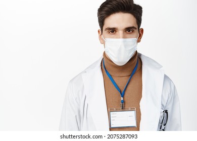 Covid 19, Quarantine. Serious Doctor In Medical Mask And Healthcare Uniform With Name Tag, Looking At Camera, Standing Over White Background