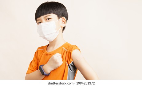 COVID 19 Vaccines For Kids Concept. Studio Portrait Of An Adorable Asian Boy With Medical Face Mask Just Got His First Dose Vaccine. Authorized, Approved, Trial, Safe, Available, Back To School.