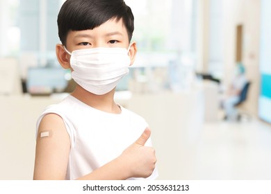 COVID 19 Vaccines For Kids Concept. Studio Portrait Of An Adorable Asian Boy With Medical Face Mask Do Thumbs Up Hand Gesture After Got His First Dose Vaccine. Immune, Safe, Available, Back To School.