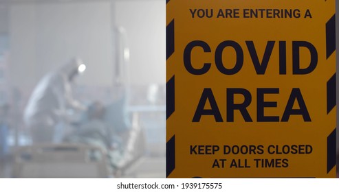 Covid Area Sign Hanging On Glass Door Of Quarantine Zone In Hospital. Doctors In Ppe Suits Treating Coronavirus Infected Patient In Isolated Ward In Modern Clinic