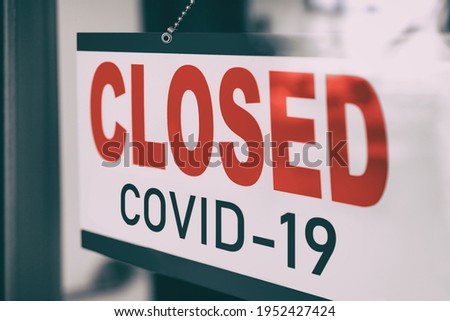 COVID Closed Sign hanging in window storefront. Government mandatory shutdown order of restaurants, non essential stores or curfew forcing closure of businesses leading to unemployment. Coronavirus.