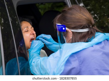 COVID or Coronavirus testing centre, UK. Asian BAME woman in a car has a coronavirus swab test with a nurse in PPE gear.