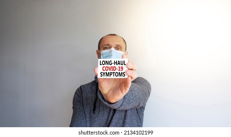 COVID Long-haul Covid Symptoms Symbol. White Card, Words Long-haul Covid-19 Symptoms. A Young Man In Grey Wear And Medical Mask. Beautiful White Background. COVID-19 Long-haul Covid Symptoms Concept.