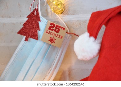 Covid Rule On Christmas Concept. Surgical Mask Hanging With Paper Tag 25 December With Red Santa Hat On Background