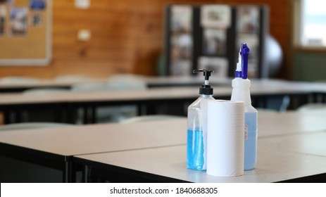 Covid Safe School Classroom Setting. Room With Students Desks And Tables. Blue Hand Sanitizer Pump Bottle And Disinfectant Spray On An Entry Table. Education Health And Safety During The Pandemic