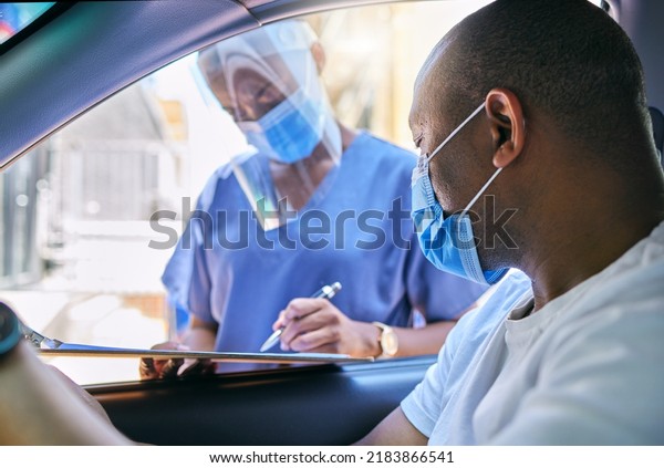 Covid testing centre and drive thru service for\
patients with coronavirus or getting vaccine. African man in car\
wearing a protective face mask to avoid contact with medical worker\
asking questions
