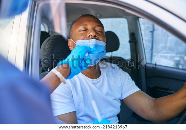 Covid\
testing and screening of a man driving in his car at a drive\
through station with medical nurse assistance. Guy getting virus\
treatment test while wearing a protective face\
mask