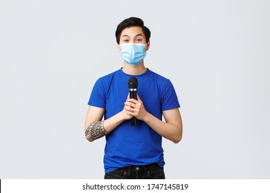 Covid019 Lifestyle, People Emotions And Leisure On Quarantine Concept. Cute Young Asian Man In Medical Mask Want Sing Song, Holding Microphone And Looking Upbeat Camera, Singing Karaoke