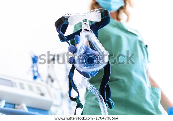 COVID19 /\
2019-ncov concept: Nurse applies a mask of the mechanical\
ventilation machine, which can be seen in the foreground. therapy\
used for lung breathing, in intensive\
care.