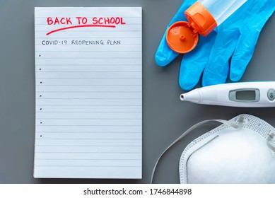 COVID-19 Back To School Reopening Plan Concept Shot. Note Pad With Medical Mask, Surgical Glove, Digital Thermometer And Hand Sanitizer