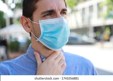 COVID-19 Close Up Man Wearing Surgical Mask With Sore Throat Outdoor. Portrait Of Man With Face Mask Against SARS-CoV-2 Suffering Throat Pain In City Street.