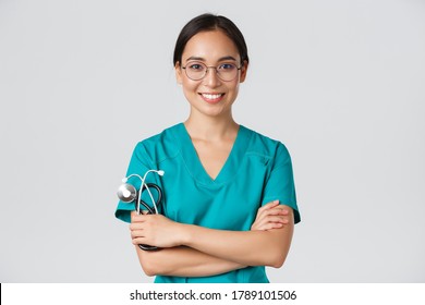Covid-19, coronavirus disease, healthcare workers concept. Close-up of confident professional female doctor, nurse in glasses and scrubs standing white background, cross arms