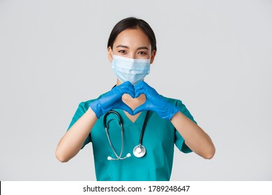 Covid-19, Coronavirus Disease, Healthcare Workers Concept. Close-up Of Charming Smiling Asian Female Doctor, Physician In Medical Mask And Rubber Gloves, Provide Care For Patients, Show Heart Gesture