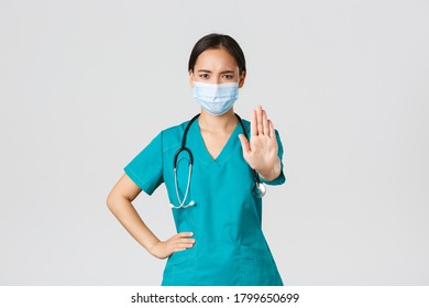 Covid-19, coronavirus disease, healthcare workers concept. Serious-looking displeased asian doctor, nurse in scrubs stopping you, show prohibit, warning gesture, forbid patient - Powered by Shutterstock