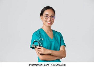 Covid-19, coronavirus disease, healthcare workers concept. Professional good-looking asian doctor, medical worker in glasses and scrubs, cross arms and smiling, white background - Shutterstock ID 1805609368